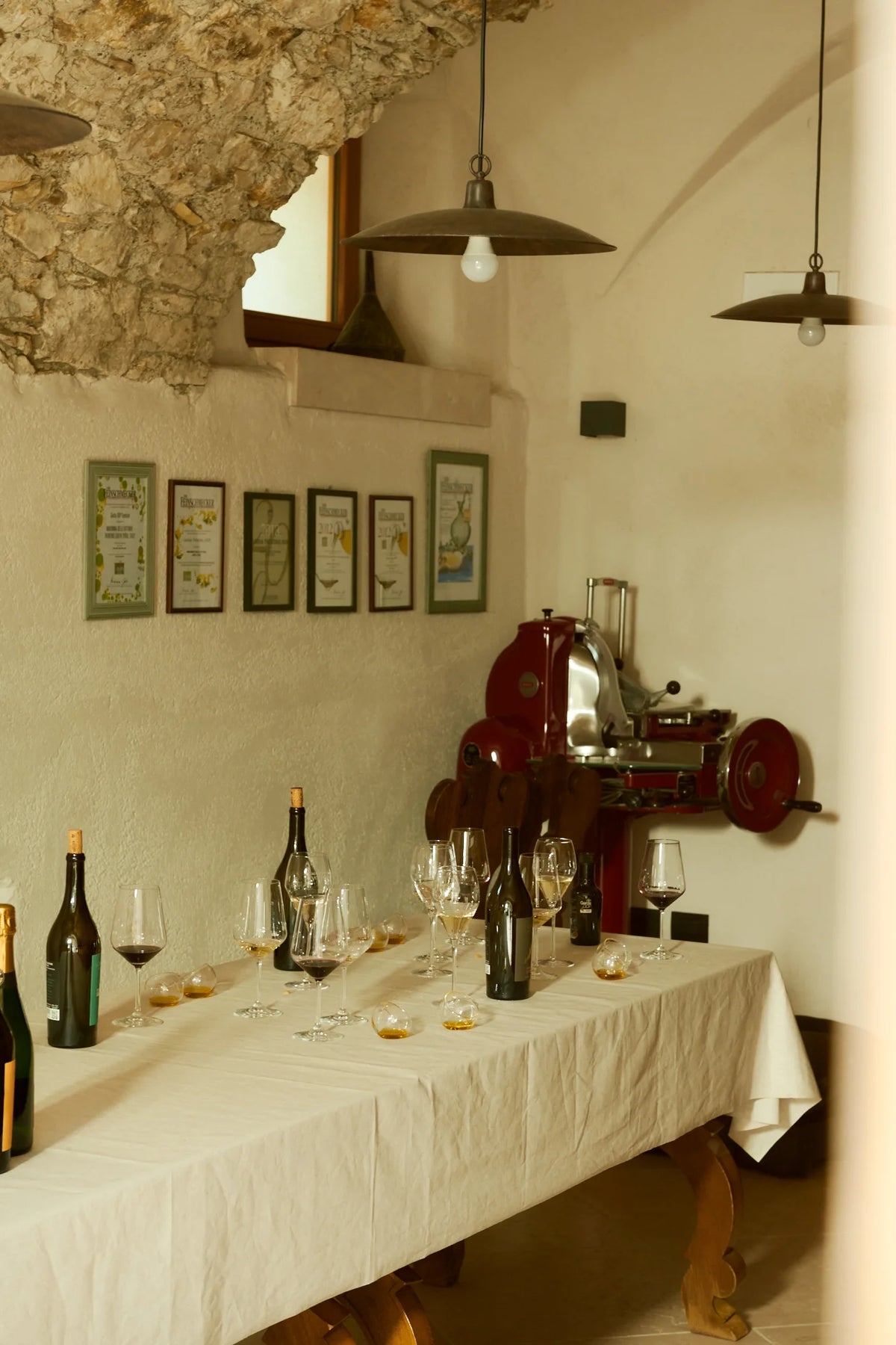 Cantina rustica in pietra con tavolo apparecchiato, bottiglie di vino e affettatrice